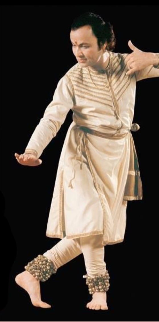 Pandit Durga Lal ji mid-pose in a cream kurta and churidar, arms extended, ghungroos at his ankles