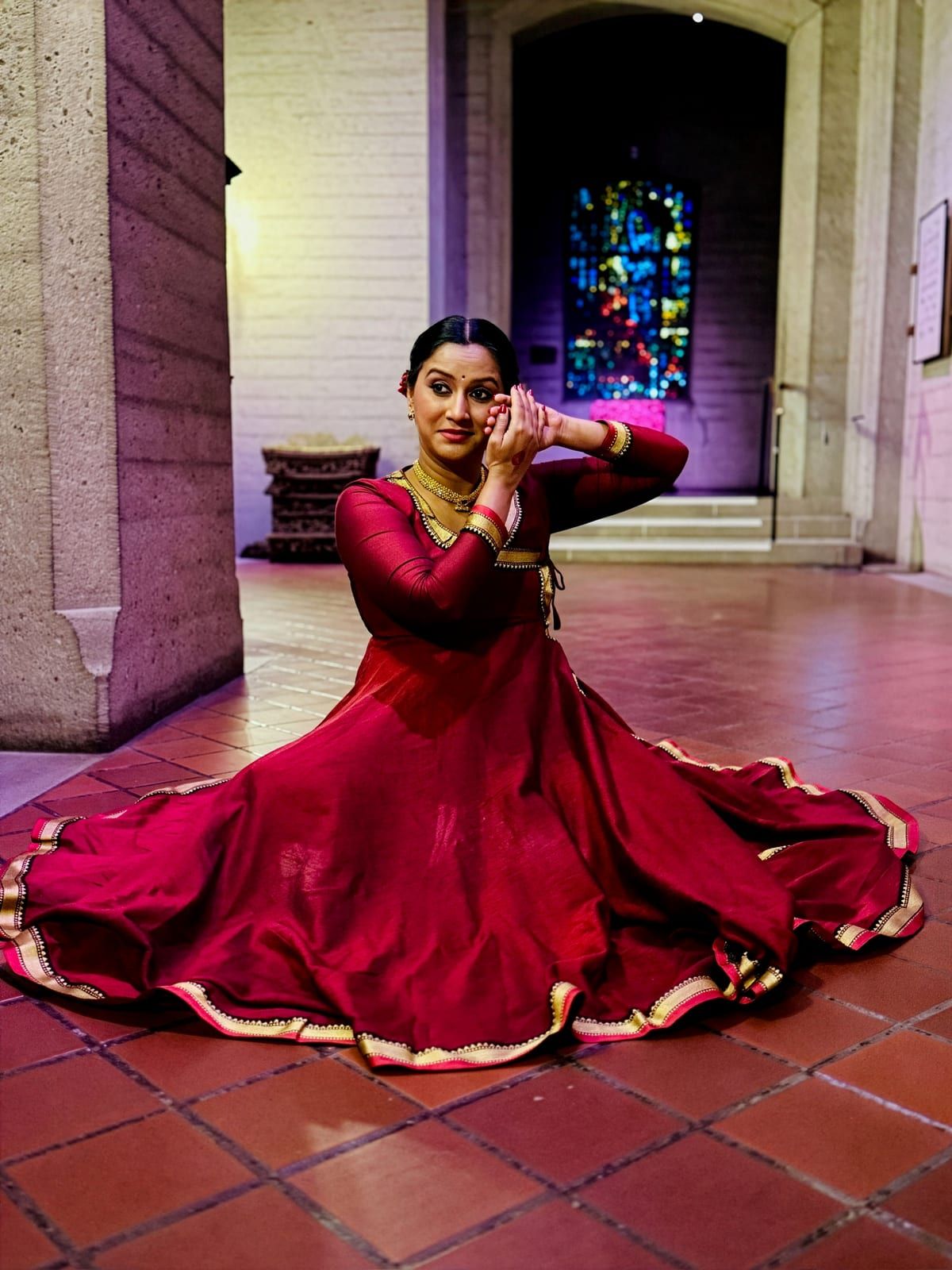 Sayali Goswami seated in a maroon anarkali with the skirt fanned around her, hands raised in a Kathak pose